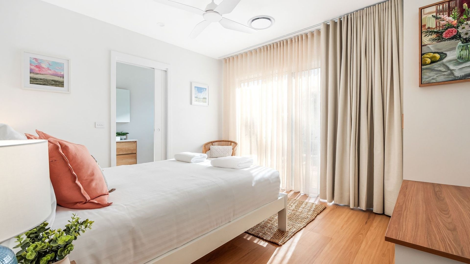 A hotel room with a bed, a desk, a chair, a ceiling fan, and a window with curtains.