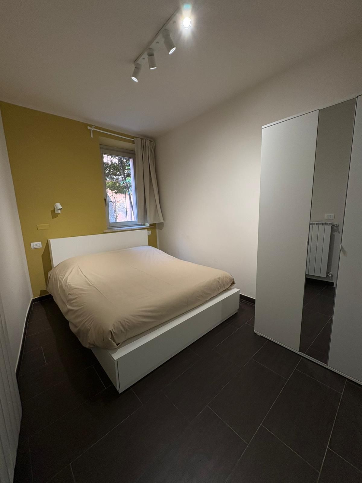 Un dormitorio con cama, armario, ventana con cortinas e iluminación en el techo.