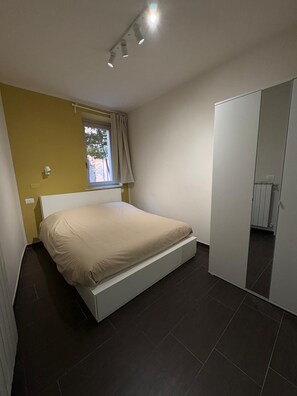 Une chambre à coucher comprenant un lit, une armoire, une fenêtre avec des rideaux et un luminaire au plafond.