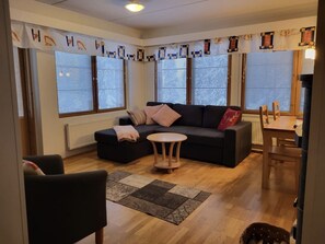 A living room with a sofa, a round coffee table, and a dining table with chairs. - Karhunvartijan Kartano B2 | 1BR Apt in Ruka Centre (Ruka)