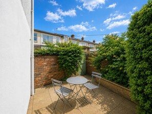 Eine Terrasse mit rundem Tisch und zwei Stühlen, umgeben von einer Backsteinmauer und Pflanzen.