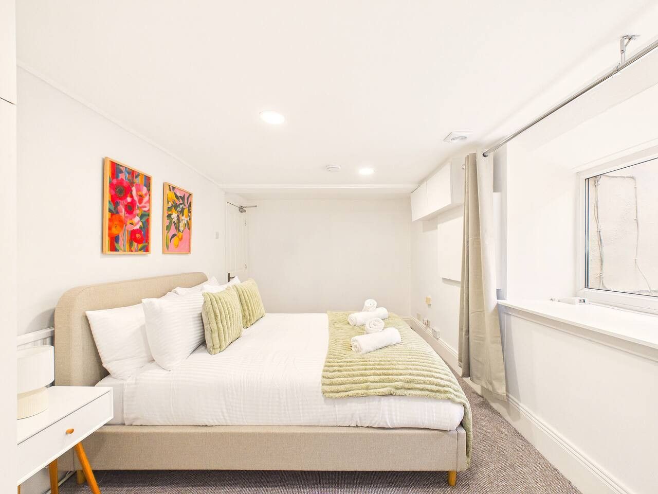 A hotel room with a bed, a bedside table, a window, and artwork on the wall.