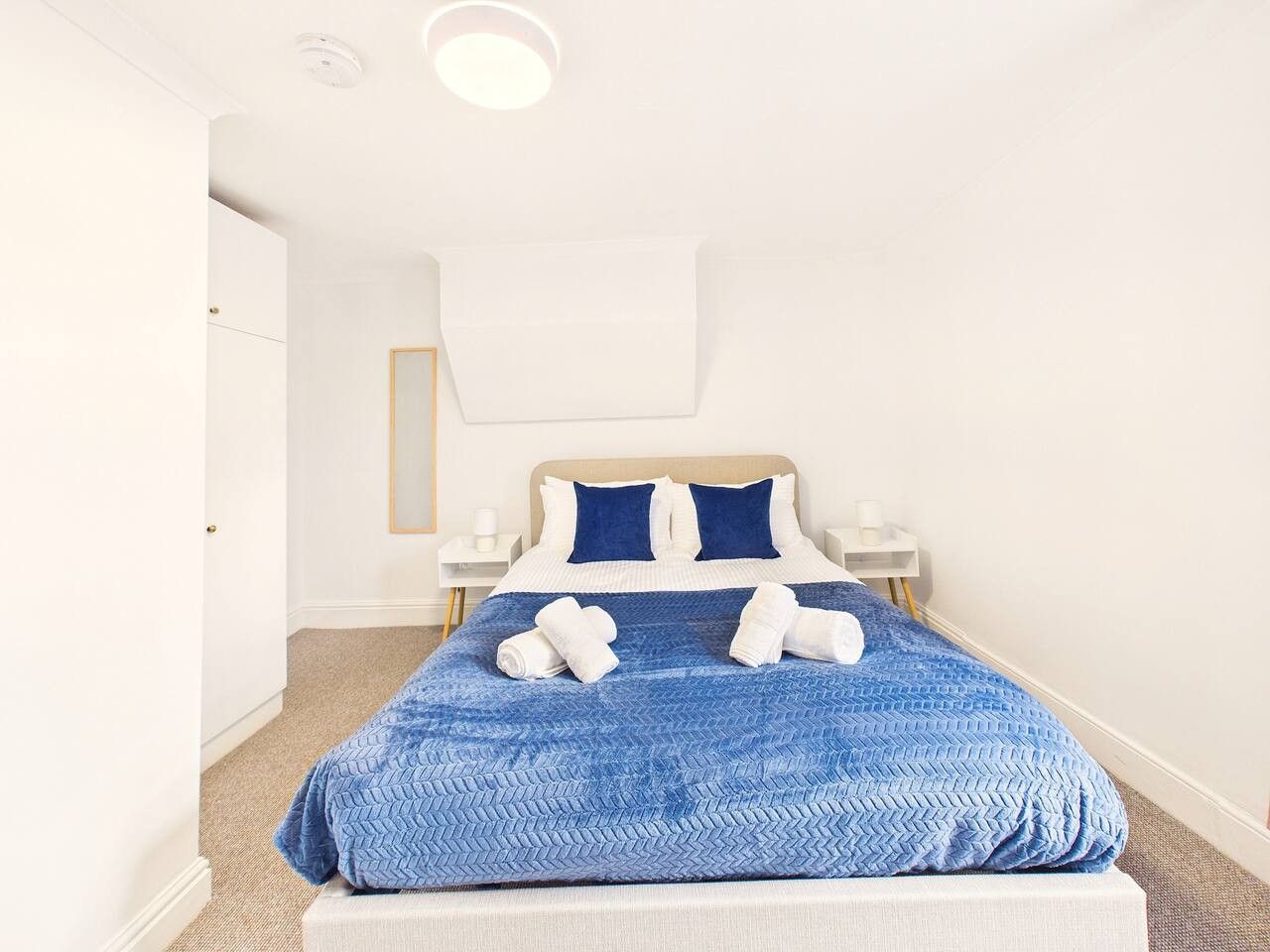 Una cama bien hecha con una colcha azul con textura, dos almohadas y dos toallas enrolladas sobre la cama.
