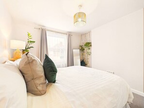 A hotel room with a bed, a bedside lamp, a mirror, and a window with curtains. - NEW Duke Street | Modern | Garden | Parking (Gloucestershire)