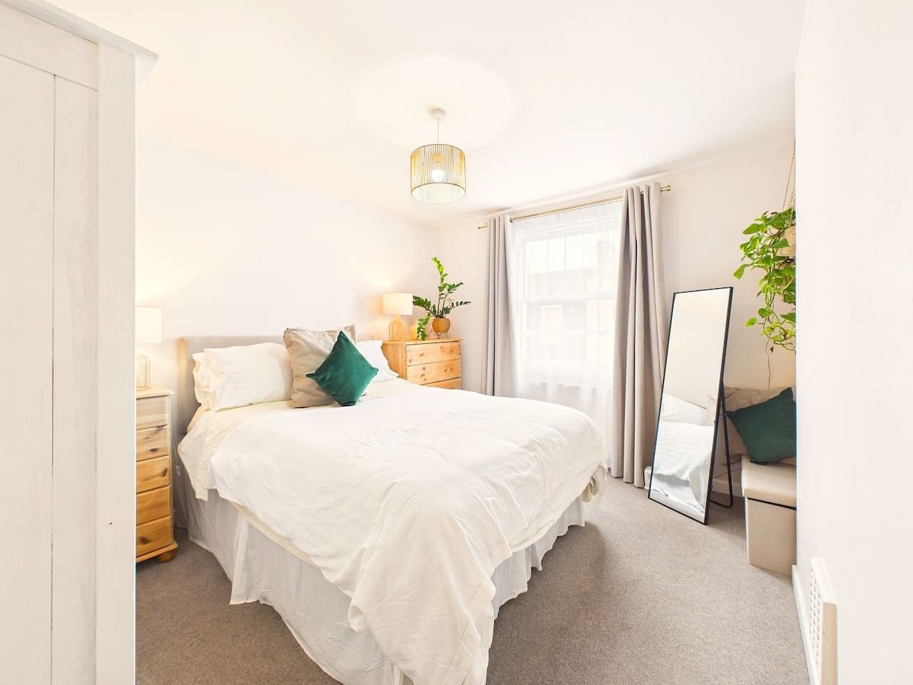 Une chambre à coucher comprenant un lit, des tables de chevet, une commode, un miroir et une fenêtre avec des rideaux.