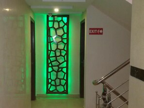 A hallway with a green-lit decorative panel, an exit sign, and a metal handrail. - Oly Saffron Near New Delhi Railway st. (New Delhi)