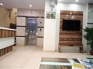 A reception area with a reception desk, a wall-mounted TV, a potted plant, and a staircase leading to an elevator. - Oly Saffron Near New Delhi Railway st. (New Delhi)
