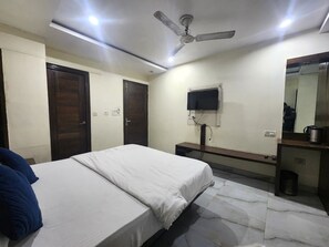 Ein Schlafzimmer mit einem Bett, einem Deckenventilator, einem an der Wand befestigten Fernseher und einem Spiegel über einem Waschbecken.