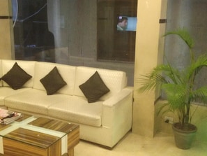 Un sofá blanco con tres cojines oscuros, una mesa de centro de madera y una planta en maceta.