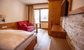 A hotel room with a bed, a red sofa, a small table, and a wooden cabinet. - Hotel Dax by Alpeffect Hotels (Lofer)