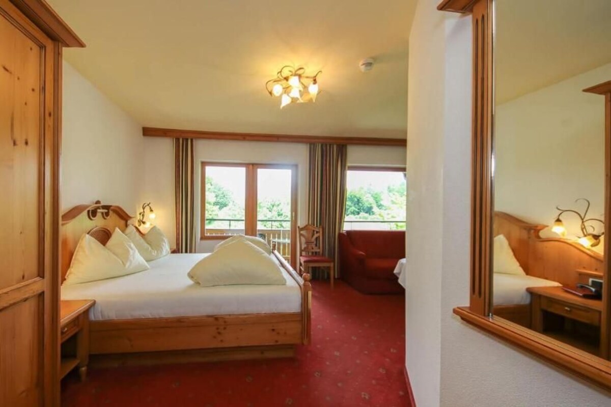Habitación de hotel con cama de madera, alfombra roja, balcón y un espejo grande.