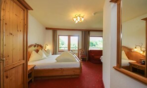 Habitación de hotel con cama de madera, alfombra roja, balcón y un espejo grande.