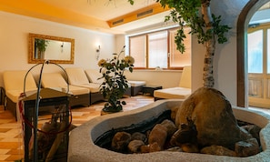 A cozy living room with a fireplace, a sofa, a coffee table, and a decorative plant. - Hotel Dax by Alpeffect Hotels (Lofer)