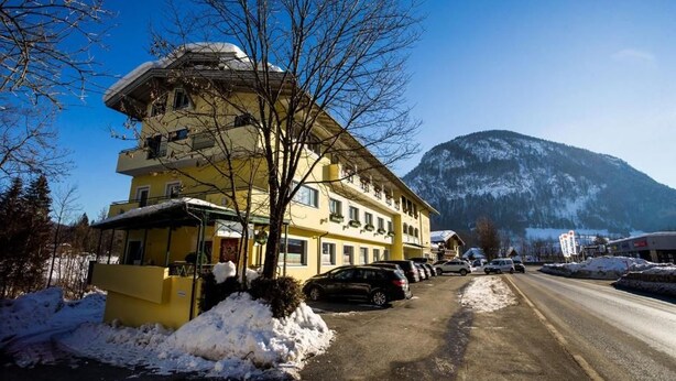 A multi-story hotel with a snow-covered ground, parked cars, and a mountain in the background. - Hotel Dax by Alpeffect Hotels (Lofer)