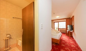 Habitación de hotel con ducha, cama, televisión y alfombra roja.