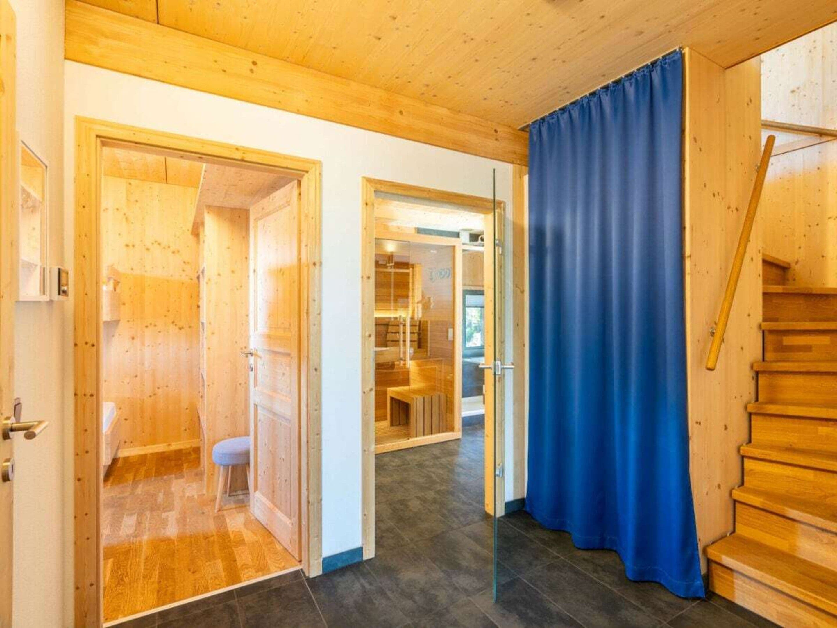 A wooden interior with a staircase, a blue curtain, and a door leading to another room.