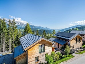 Eine Reihe von Holzhütten mit geneigten Dächern, umgeben von einem Wald und Bergen im Hintergrund.
