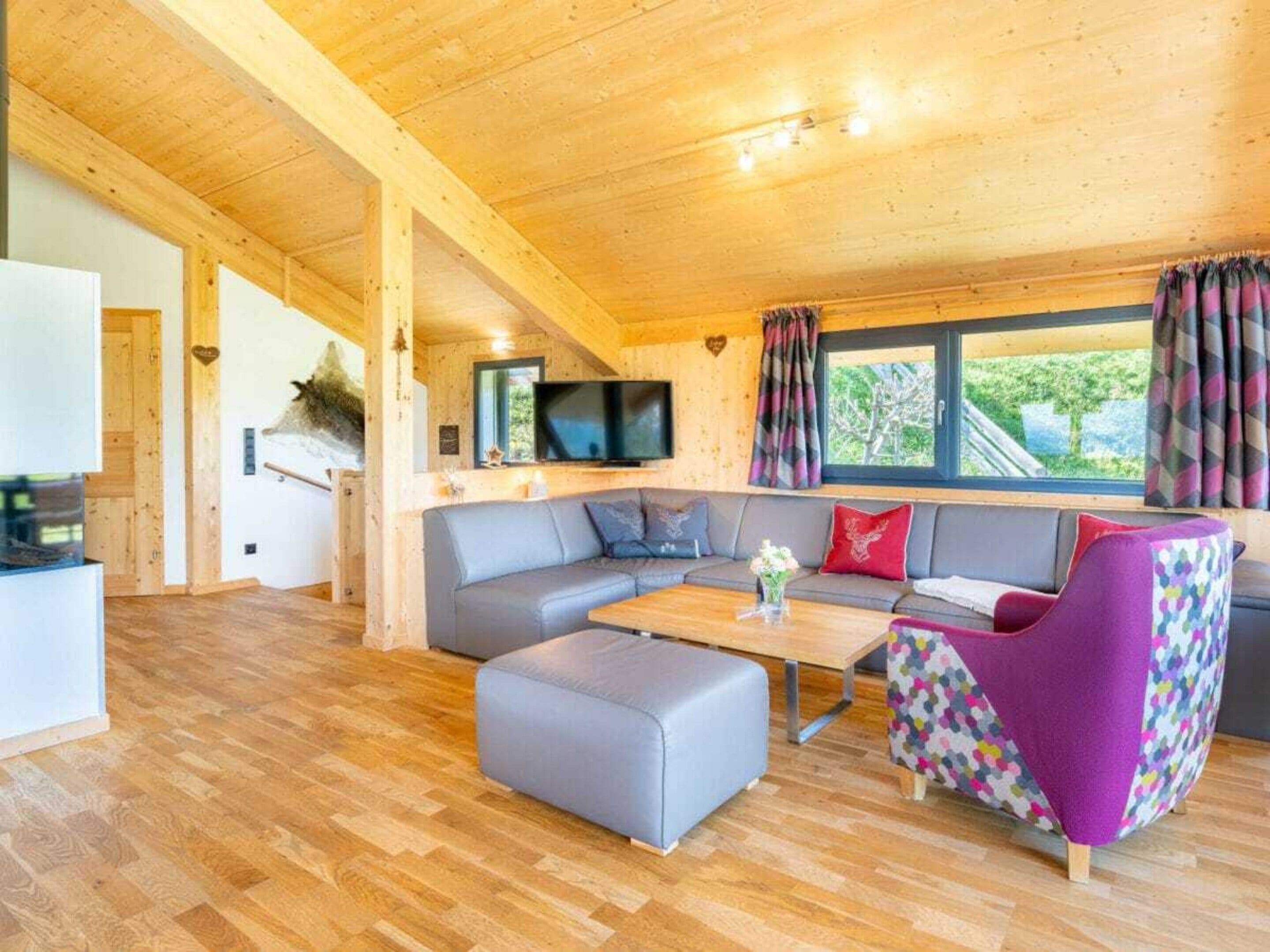 A cozy cabin interior with a wooden ceiling, a sofa set, a television, and a window with curtains.