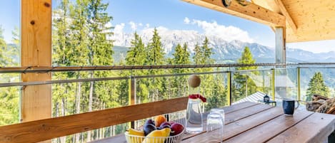 A wooden deck with a table, a bowl of fruit, a bottle, and glasses. A deer antler hangs from the ceiling.