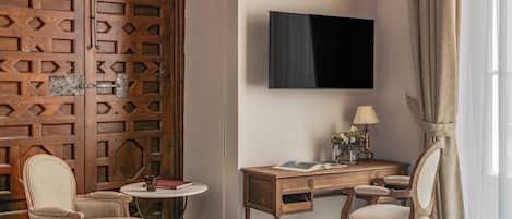 Habitació d'hotel amb un llit, escriptori, dues cadires, televisió i finestra amb cortines.