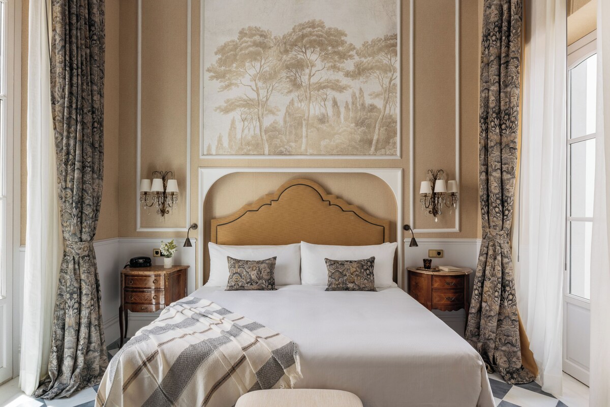 A hotel room with a large bed, two bedside tables, a headboard, and a wall-mounted painting.