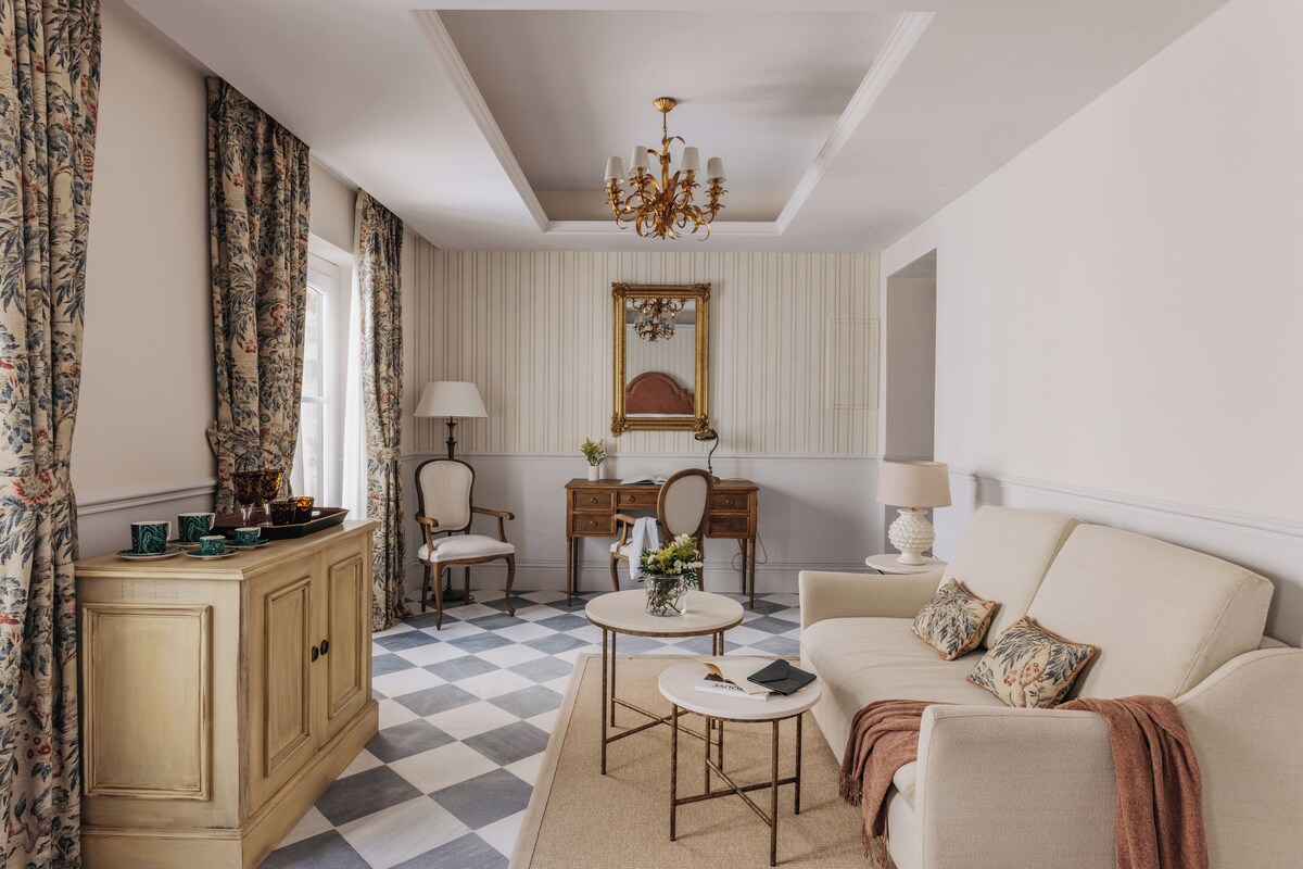 A room with a checkered floor, a sofa, a desk, a chair, a cabinet, and a chandelier.