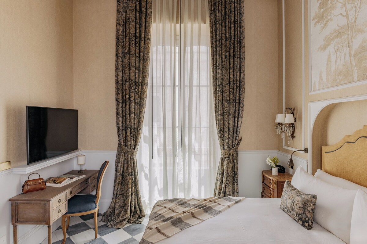 A hotel room with a bed, a desk with a chair, a television, and curtains.