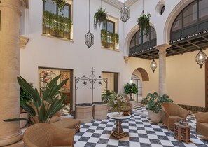 Un hall d’entrée spacieux avec un sol à carreaux, des meubles en osier et des plantes suspendues.