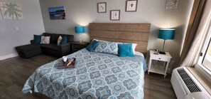 A bedroom with a bed, a sofa, a nightstand, and a lamp. - Cozy studio in soothing Daytona Beach with refreshing beachfront views (Daytona Beach)