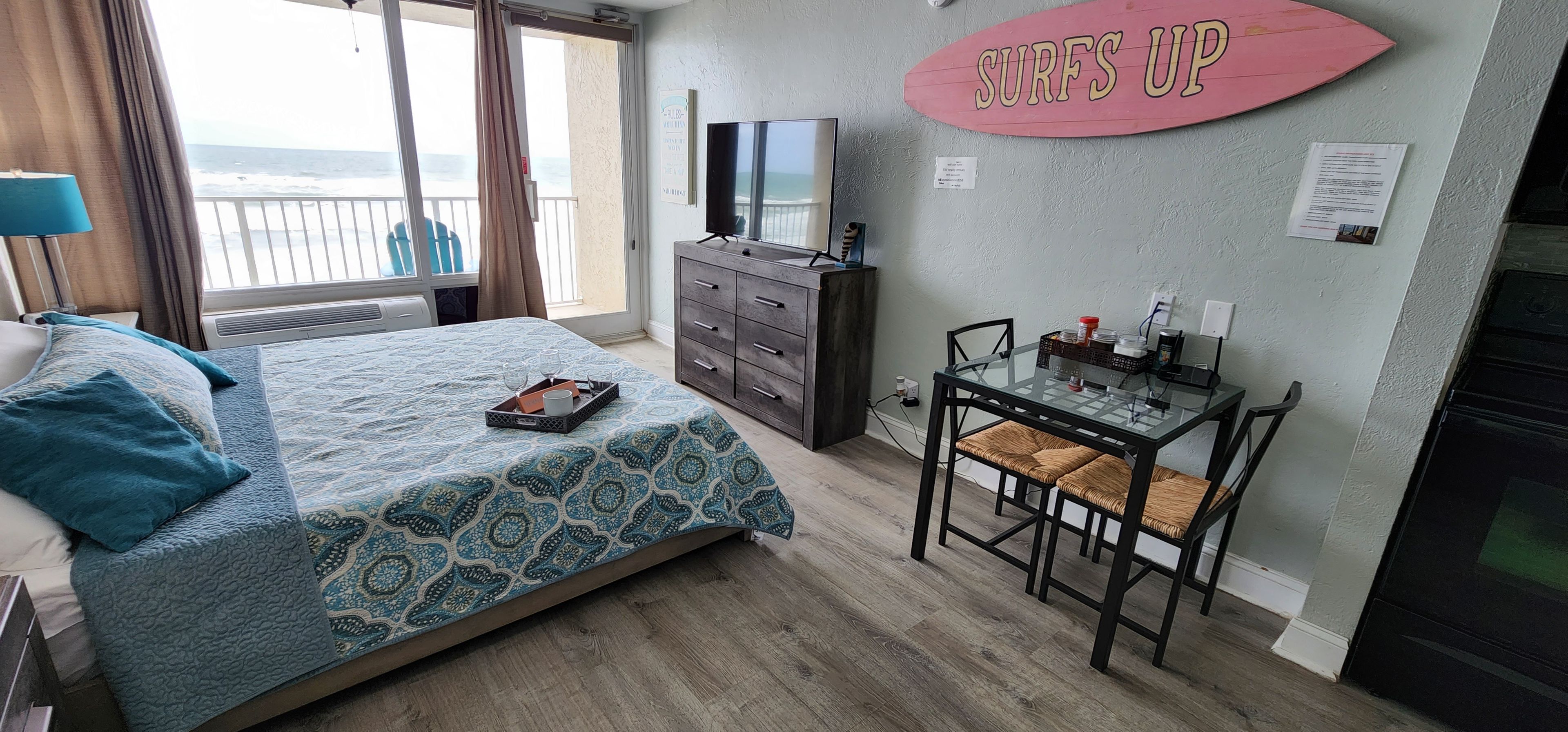 Ein Schlafzimmer mit einem Bett, einem Schreibtisch mit Stuhl, einem Fernseher und Blick aufs Meer.