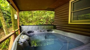 Uma banheira de hidromassagem com vários jatos, rodeada por um deck de madeira e vegetação exuberante.