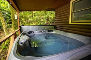 Un bain à remous doté de plusieurs jets, entouré d’une terrasse en bois et d’une végétation luxuriante.