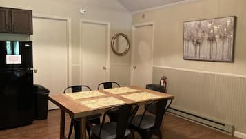 Un comedor con una mesa de madera, cuatro sillas, un refrigerador negro y un cuadro en la pared.