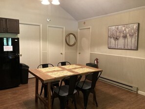 Un coin repas avec une table en bois, quatre chaises, un réfrigérateur noir et un tableau accroché au mur.