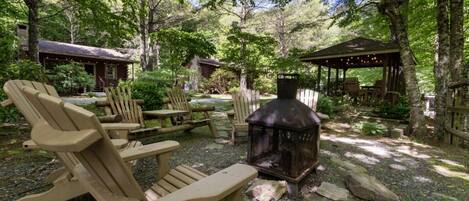 Un espace extérieur boisé, aménagé avec des fauteuils Adirondack, un poêle à bois et des structures en bois.