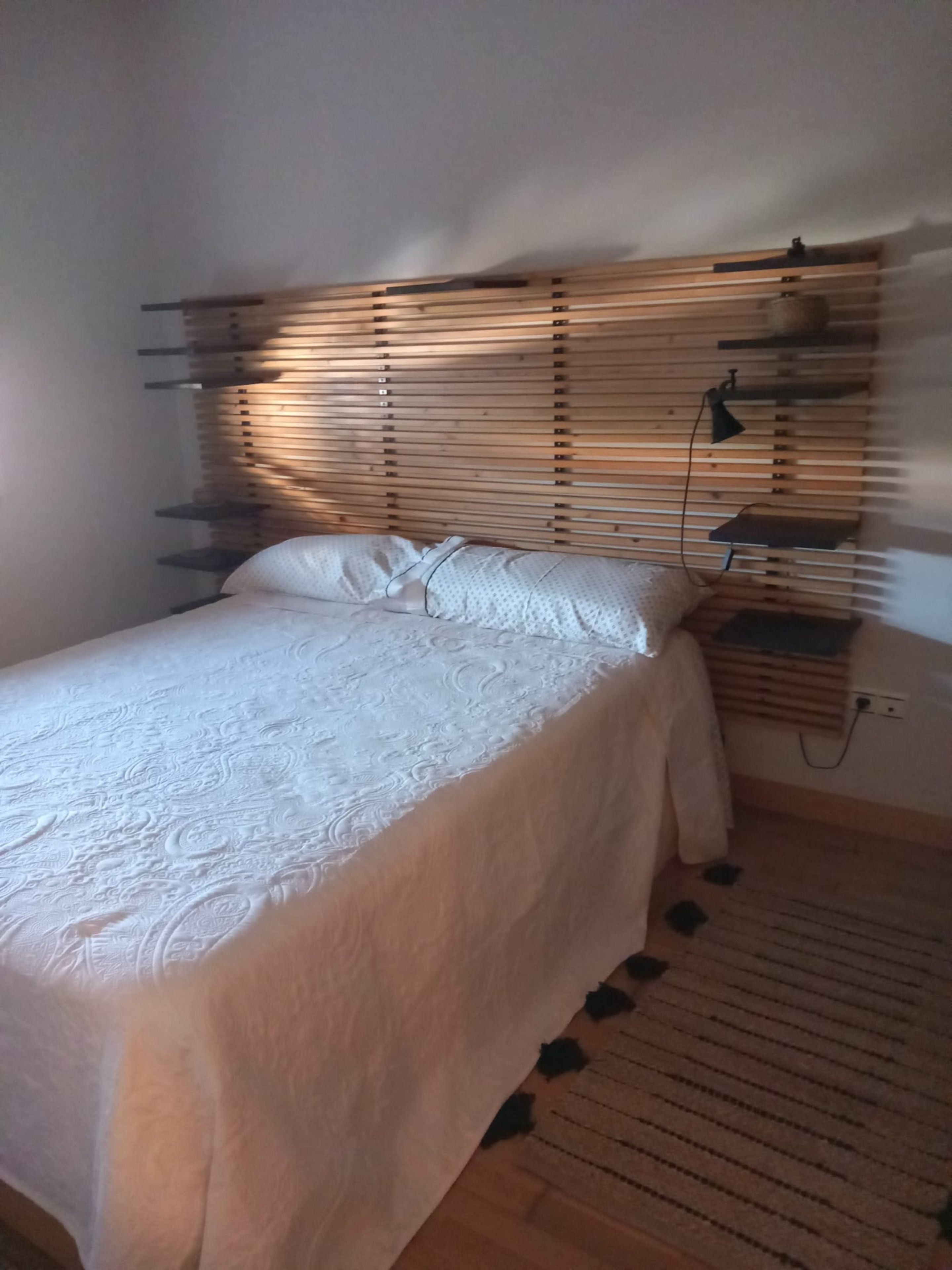Un dormitorio con cama, detalles de madera en la pared, una mesita de noche y una lámpara.