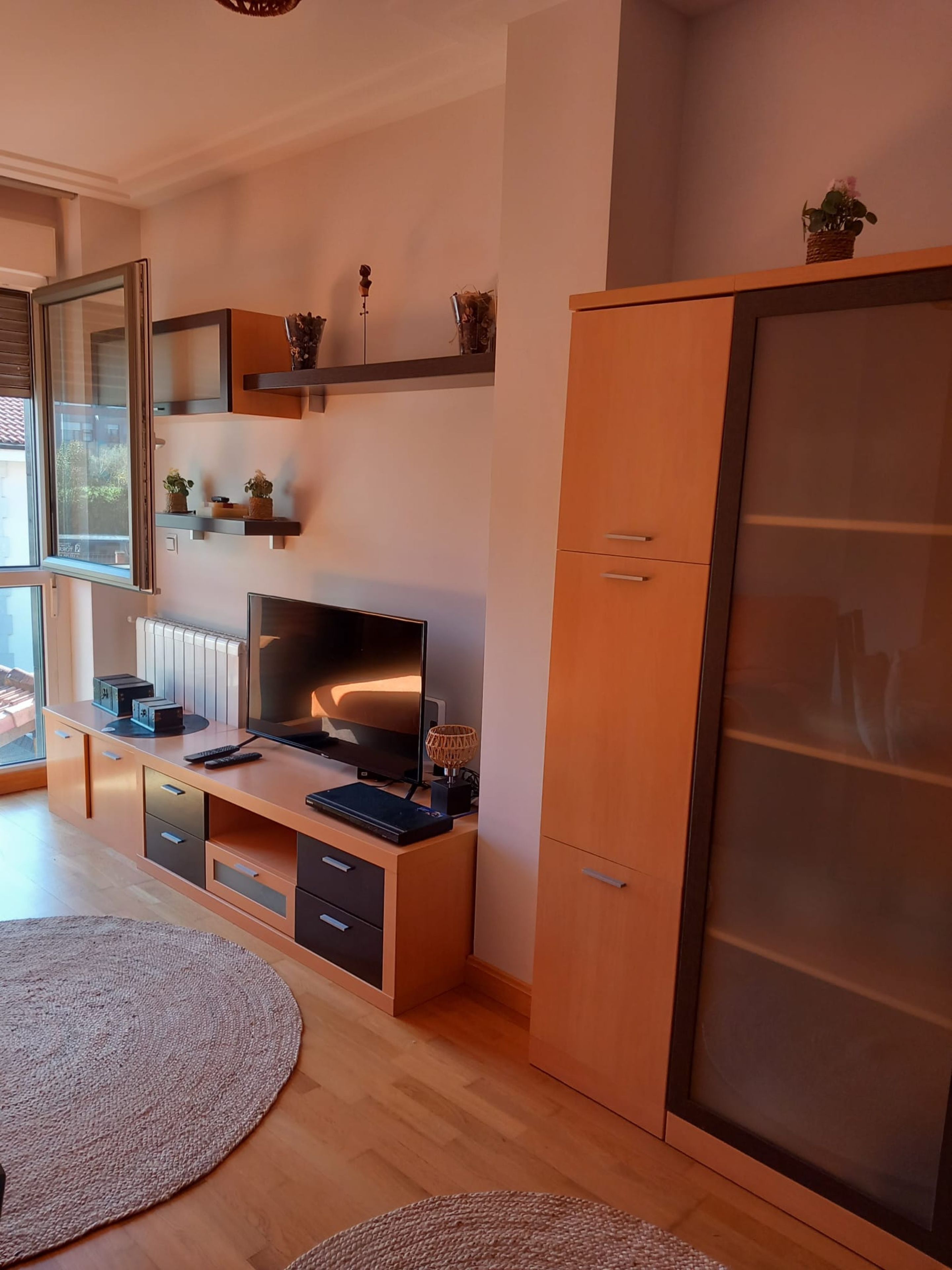 Una sala de estar moderna con un televisor grande, muebles de madera y un amplio armario.