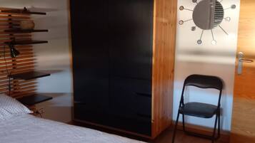A bedroom with a bed, a wardrobe, a chair, and a wall-mounted light fixture.