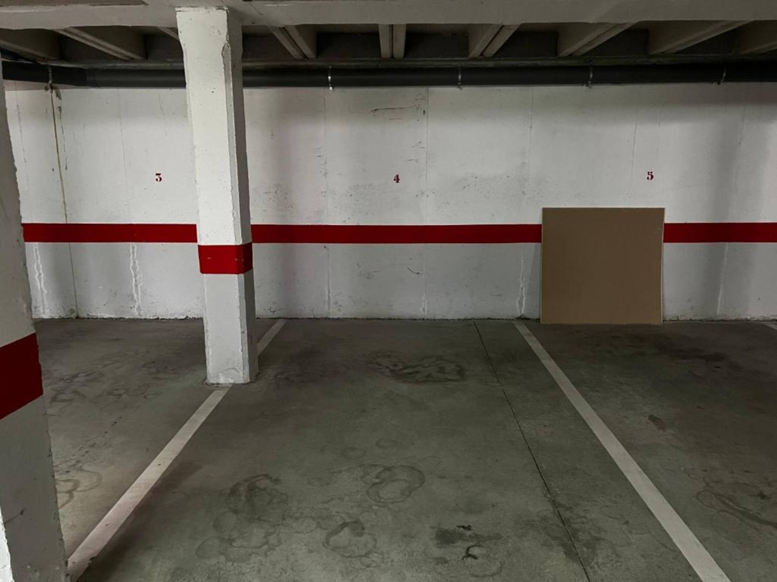 A parking garage with concrete floors, white walls, and red stripes.