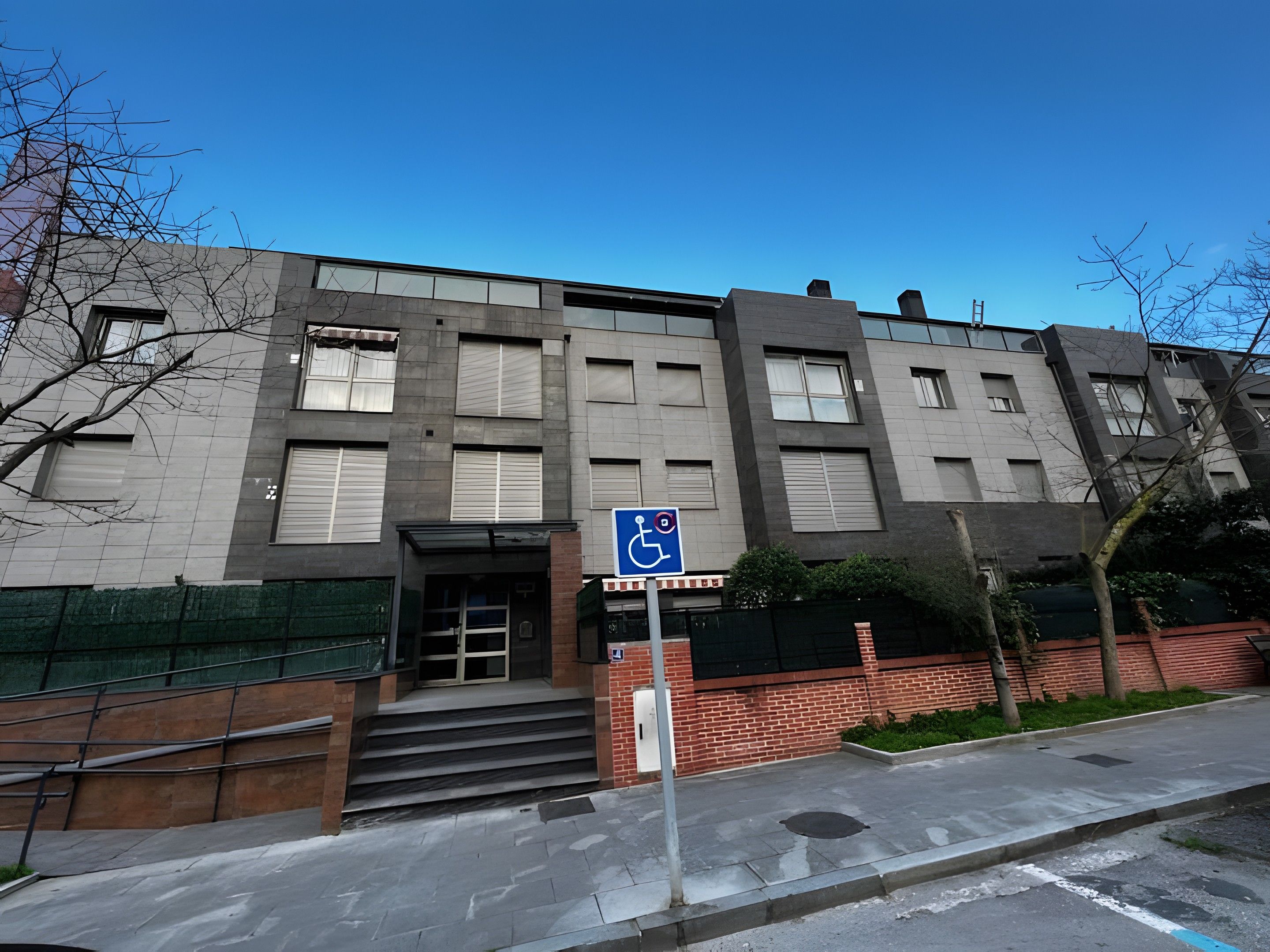 A multi-story building with a wheelchair-accessible entrance, a brick facade, and a clear blue sky.