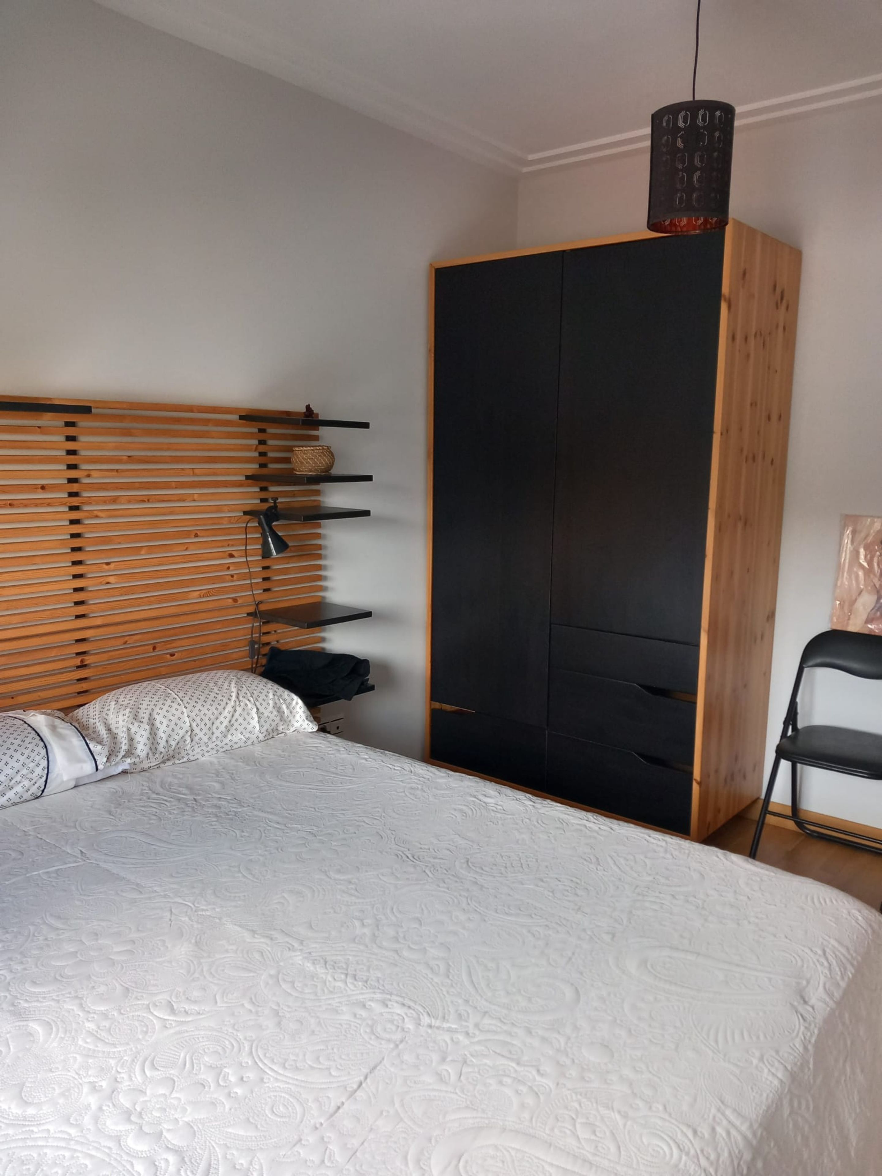 A bedroom with a bed, a wooden headboard, a wardrobe, and a chair.