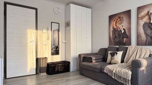 A modern living room with a grey sofa, a black ottoman, a white wardrobe, and a large mirror. - The 6th - Studio Apartment Porta Venezia (Milan)