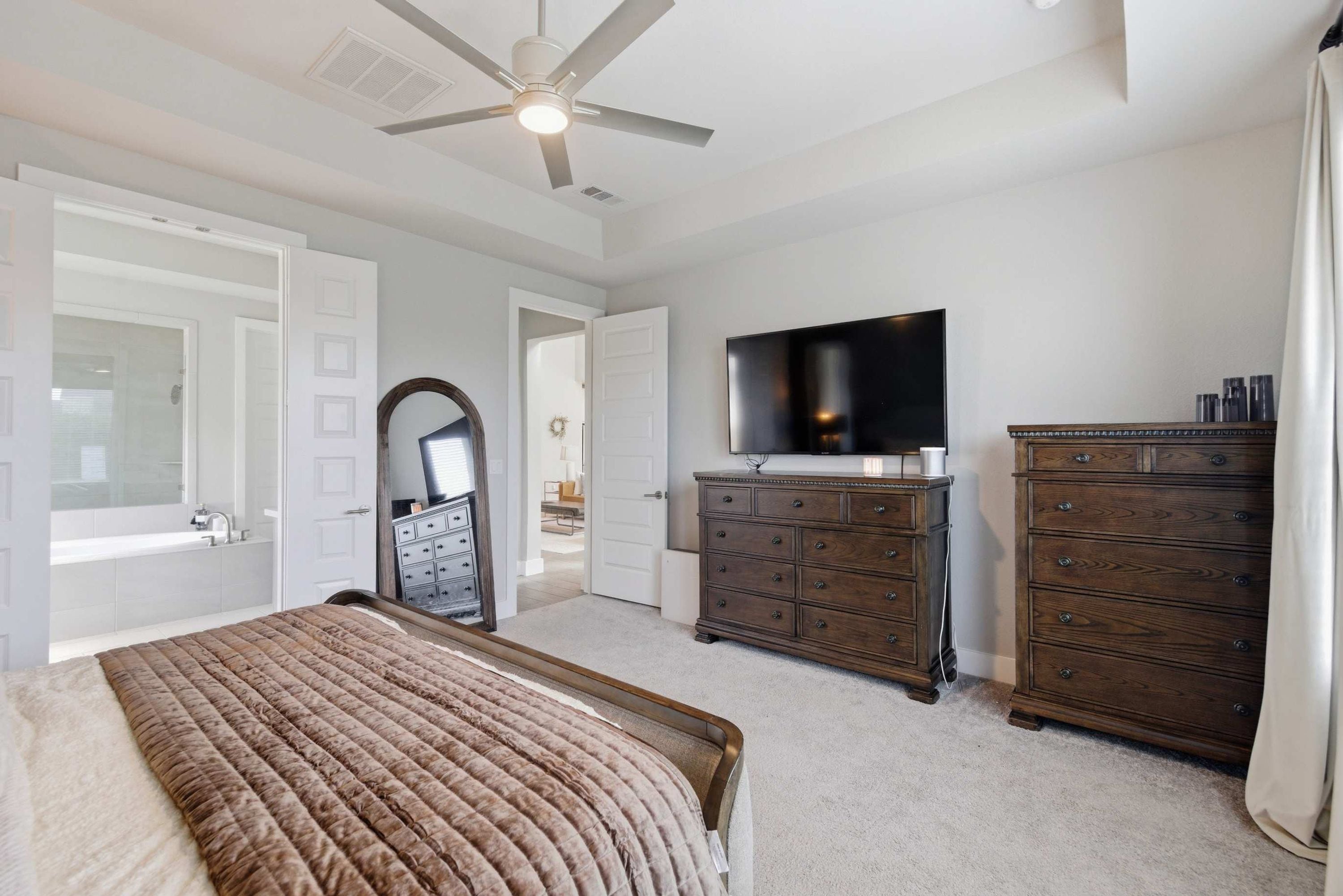 A bedroom with a bed, a dresser, a television, and a ceiling fan.