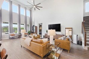 A spacious living room with a large sofa, a coffee table, and a TV mounted on the wall. - Easton Park 4BR With Private Resort-style Pool (Austin)
