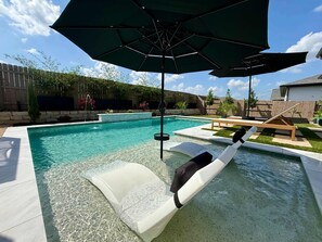 A swimming pool with clear water, a lounge chair, and an umbrella. - Easton Park 4BR With Private Resort-style Pool (Austin)