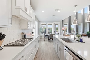 A modern kitchen with white cabinetry, a central island, and a dining area with a table and chairs. - Easton Park 4BR With Private Resort-style Pool (Austin)