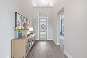 A hallway with a wooden console table, a vase with flowers, a framed picture of dogs, and a door with frosted glass panels. - Easton Park 4BR With Private Resort-style Pool (Austin)