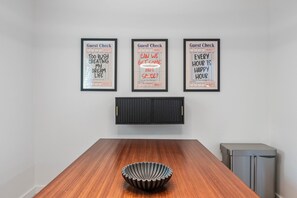 A dining area with a wooden table and a black bowl in the center. Three framed 'Guest Check' signs are hung on the wall above the table. - Vaulted Ceilings Home With 2 000-book Library (Austin)