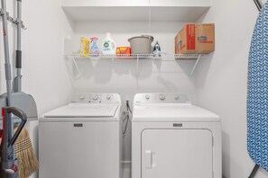 A laundry room with two Maytag washing machines, a shelf with cleaning supplies, and a broom. - Vaulted Ceilings Home With 2 000-book Library (Austin)