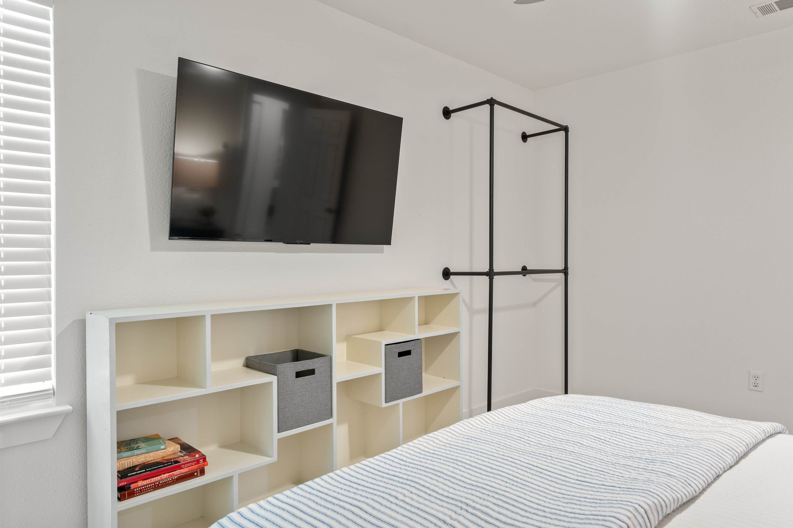 A bedroom with a bed, a TV mounted on the wall, a wardrobe, and a shelf unit with storage boxes.